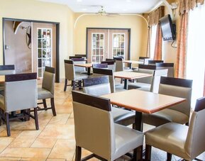 Bright hotel dining area with multiple tables, chairs, television, and large windows at Comfort Suites San Antonio SeaWorld - Lackland AFB.