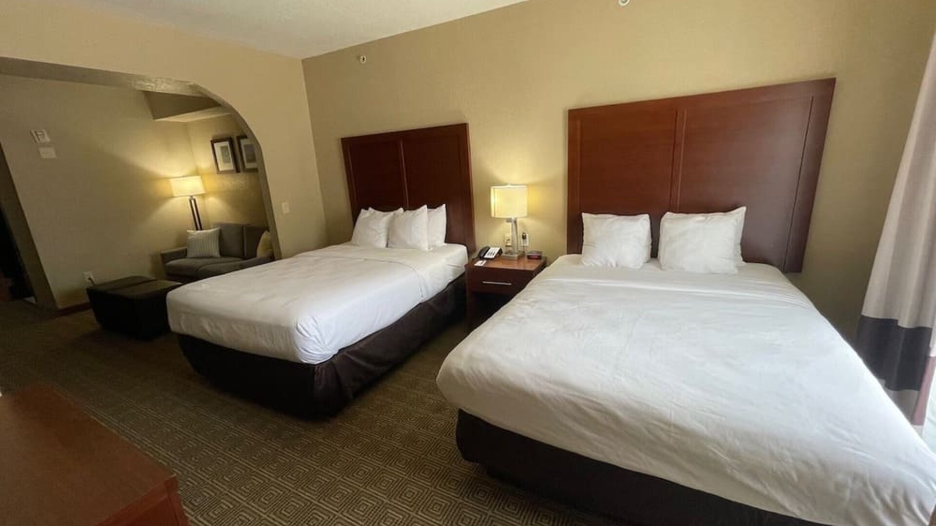 Spacious guest suite with two beds, bedside lighting, and a separate seating area with sofa and ottoman at Comfort Suites San Antonio SeaWorld - Lackland AFB.