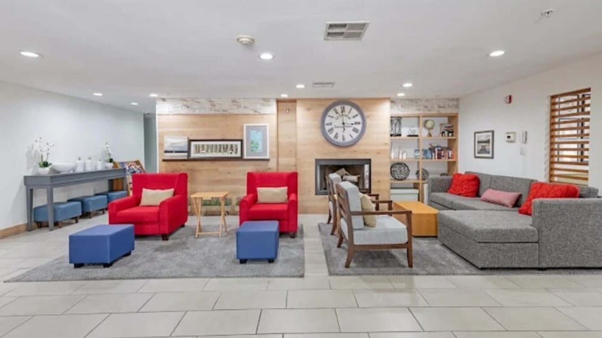 Hotel lobby with sofas, red armchairs, ottomans, fireplace, wall clock, and lounge seating at SureStay by Best Western Lewisville Dallas.
