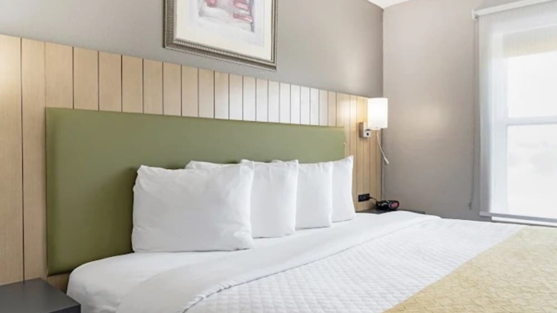 Close-up of king bed with white bedding, green upholstered headboard, bedside lighting, and large window at SureStay by Best Western Lewisville Dallas.