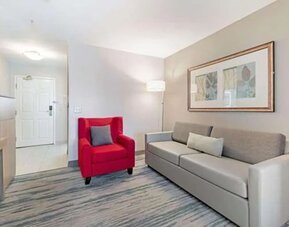 Guest suite seating area with sofa, red armchair, floor lamp, and framed artwork at SureStay by Best Western Lewisville Dallas.