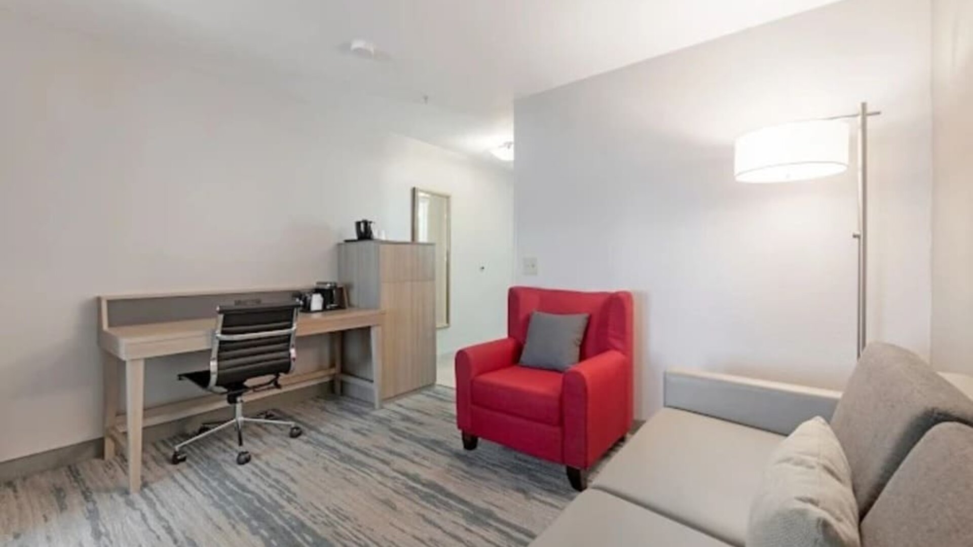 Guest suite workspace with desk, office chair, storage cabinet, red armchair, sofa, and floor lamp at SureStay by Best Western Lewisville Dallas.