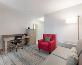 Guest suite workspace with desk, office chair, storage cabinet, red armchair, sofa, and floor lamp at SureStay by Best Western Lewisville Dallas.