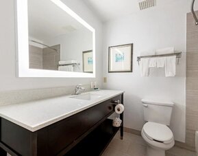 Guest bathroom with illuminated mirror, vanity, toilet, towels, and tiled bath area at SureStay by Best Western Lewisville Dallas.