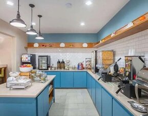 Breakfast buffet with waffle makers, cereal dispensers, hot-food station, beverages, and blue cabinetry at SureStay by Best Western Lewisville Dallas.