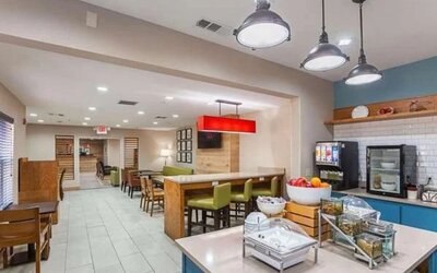 Breakfast and dining area with buffet station, tables, chairs, pendant lighting, and counter seating at SureStay by Best Western Lewisville Dallas.