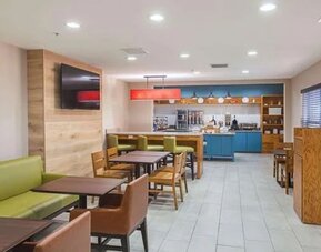 Hotel dining area with tables, chairs, booth seating, television, and breakfast station at SureStay by Best Western Lewisville Dallas.