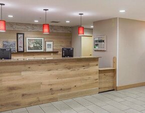 Reception area with wood-panelled front desk, red pendant lights, framed artwork, and bookcase at SureStay by Best Western Lewisville Dallas.