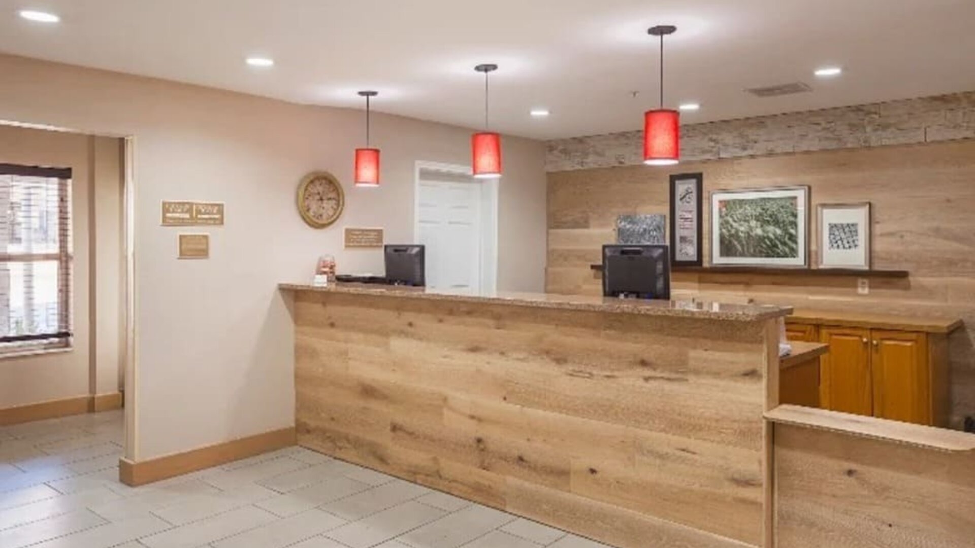 Front desk with wood-panelled reception counter, computer stations, red pendant lighting, and wall décor at SureStay by Best Western Lewisville Dallas.