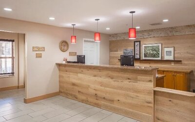 Front desk with wood-panelled reception counter, computer stations, red pendant lighting, and wall décor at SureStay by Best Western Lewisville Dallas.