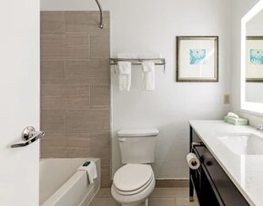 Guest bathroom with bathtub and shower, tiled wall, toilet, towels, vanity, and illuminated mirror at SureStay by Best Western Lewisville Dallas.