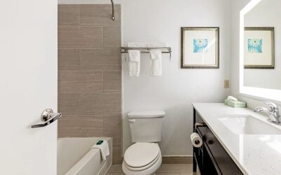 Guest bathroom with bathtub and shower, tiled wall, toilet, towels, vanity, and illuminated mirror at SureStay by Best Western Lewisville Dallas.
