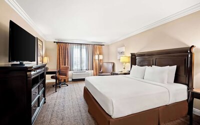 King guest room with white bedding, dark wood furnishings, television, desk, and seating area at Best Western Ontario Mills Mall.