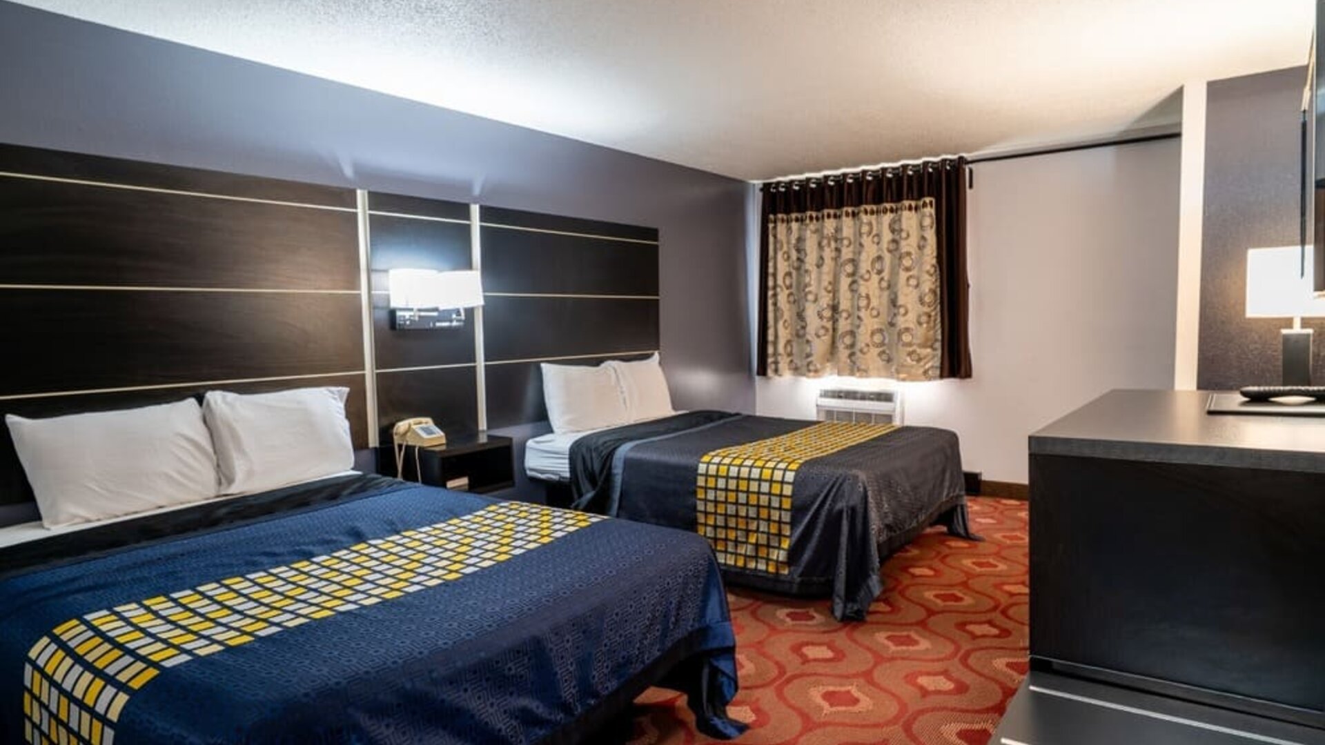 Guest room with two beds, patterned bedding, window, and dark wood furnishings at Coratel Inn & Suites By Jasper Hastings.