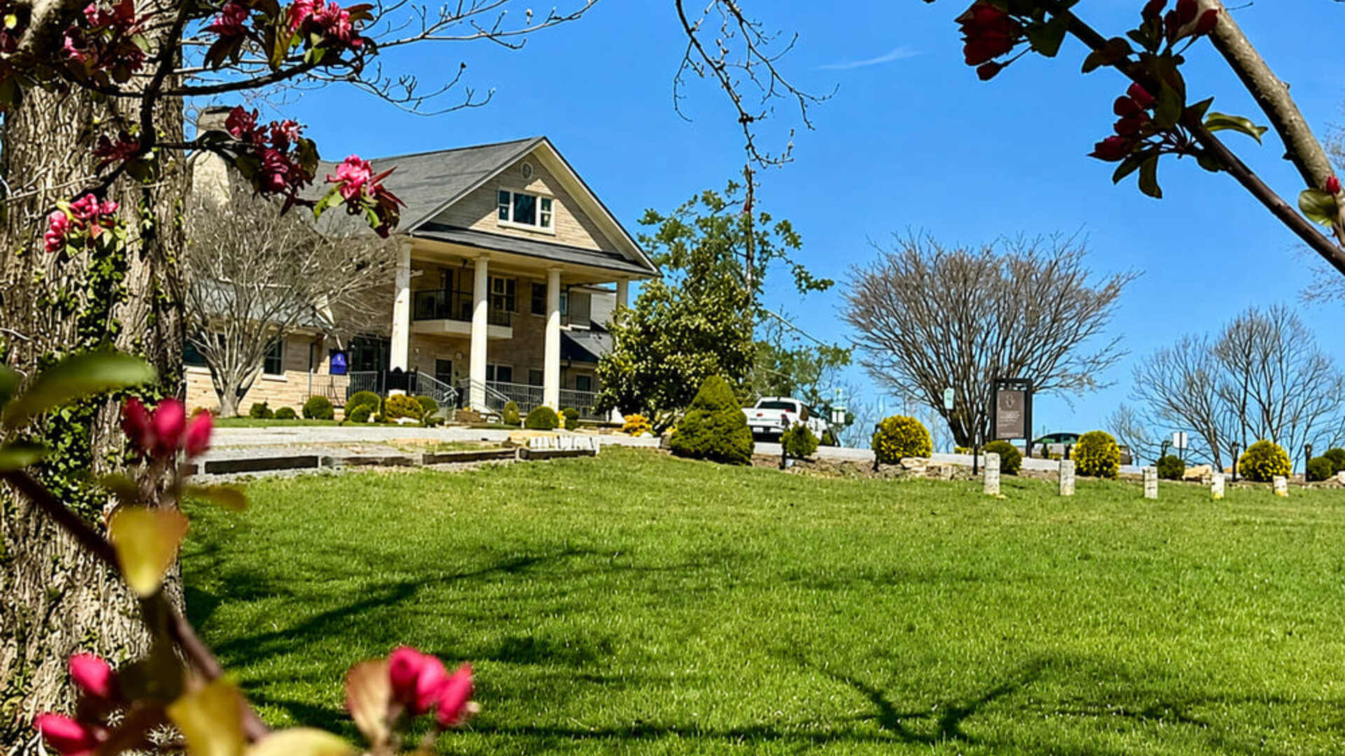 Exterior view of the main building at SKYLARANNA Resort & Spa, surrounded by landscaped lawns, mature trees, and flowering plants.