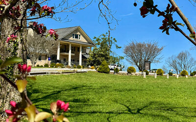 Exterior view of the main building at SKYLARANNA Resort & Spa, surrounded by landscaped lawns, mature trees, and flowering plants.