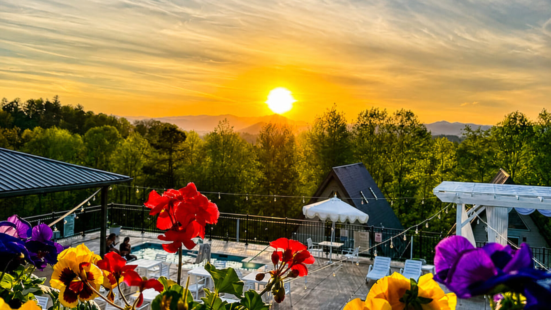 Scenic sunset view over the pool area and surrounding mountains, framed by colourful flowers at SKYLARANNA Resort & Spa.