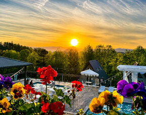 Scenic sunset view over the pool area and surrounding mountains, framed by colourful flowers at SKYLARANNA Resort & Spa.