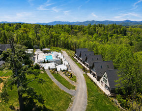 Aerial view of SKYLARANNA Resort & Spa, showing the pool complex, chalet-style accommodation, wooded grounds, and surrounding mountain landscape.