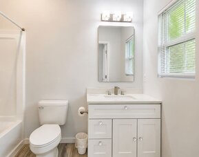 Bright guest bathroom featuring a vanity, mirror, toilet, window, and bathtub at SKYLARANNA Resort & Spa.