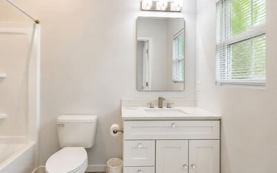 Bright guest bathroom featuring a vanity, mirror, toilet, window, and bathtub at SKYLARANNA Resort & Spa.