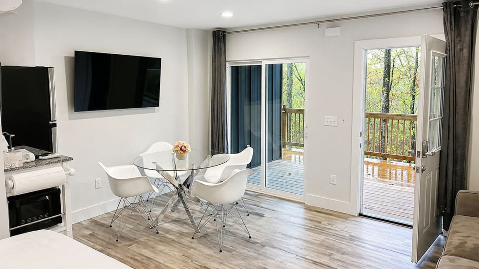 Bright guest accommodation featuring a dining area, wall-mounted TV, kitchenette, and direct access to an outdoor balcony at SKYLARANNA Resort & Spa.