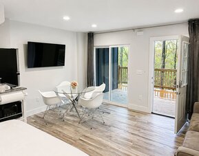 Bright guest accommodation featuring a dining area, wall-mounted TV, kitchenette, and direct access to an outdoor balcony at SKYLARANNA Resort & Spa.