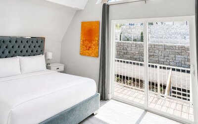 Bright cabin bedroom at SKYLARANNA Resort & Spa, featuring a queen bed, tufted headboard, colourful artwork, vaulted ceiling, and sliding glass doors.