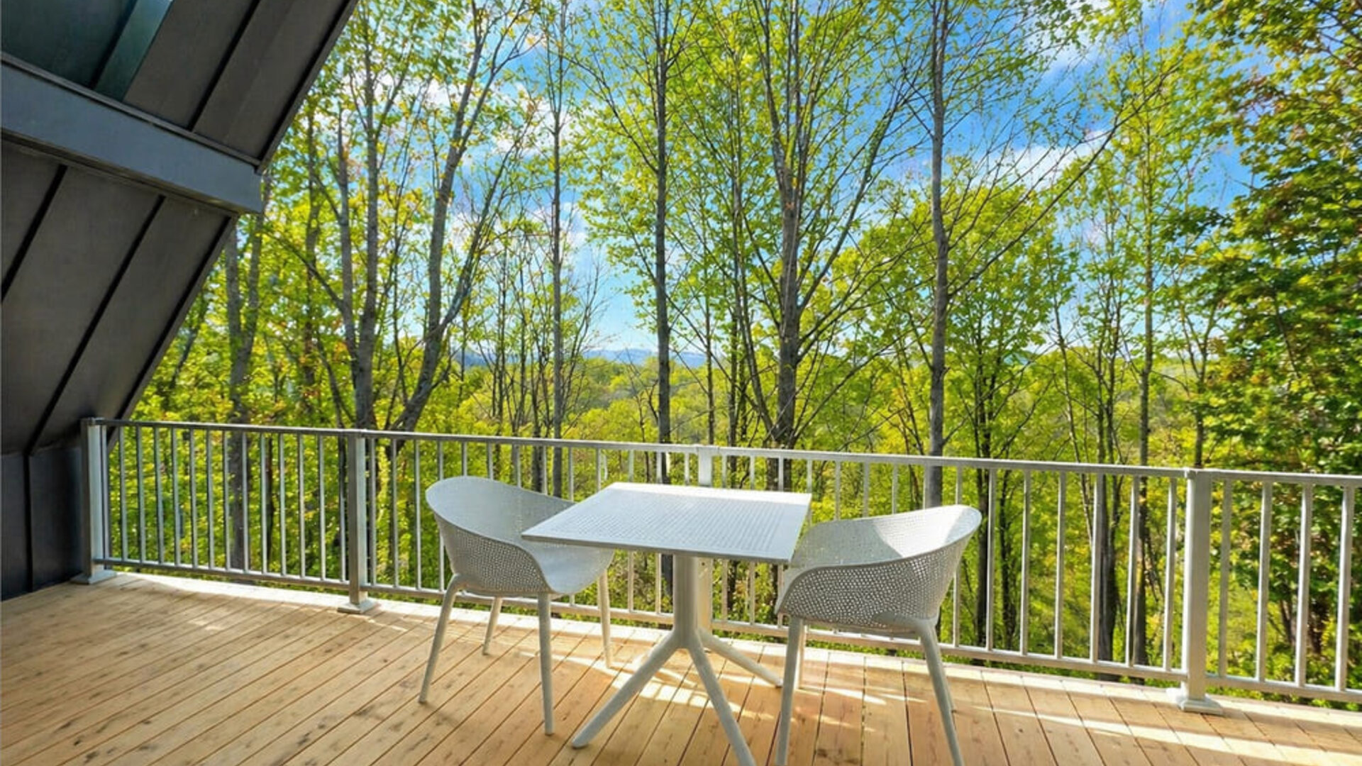Private wooden balcony at SKYLARANNA Resort & Spa, furnished with a table and chairs and overlooking the surrounding woodland.