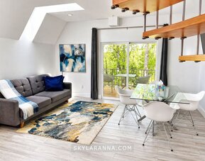 Open-plan cabin living and dining area at SKYLARANNA Resort & Spa, featuring a sofa, glass dining table, contemporary artwork, spiral staircase, and doors opening onto a private balcony.