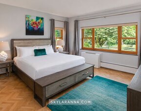 Guest room at SKYLARANNA Resort & Spa, featuring a king bed, contemporary furnishings, colourful artwork, large windows, and views of the surrounding greenery.
