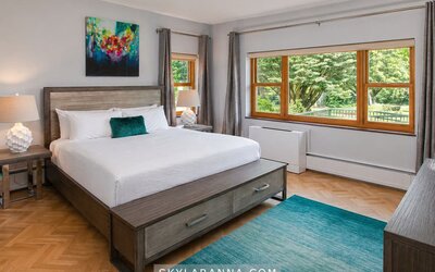 Guest room at SKYLARANNA Resort & Spa, featuring a king bed, contemporary furnishings, colourful artwork, large windows, and views of the surrounding greenery.