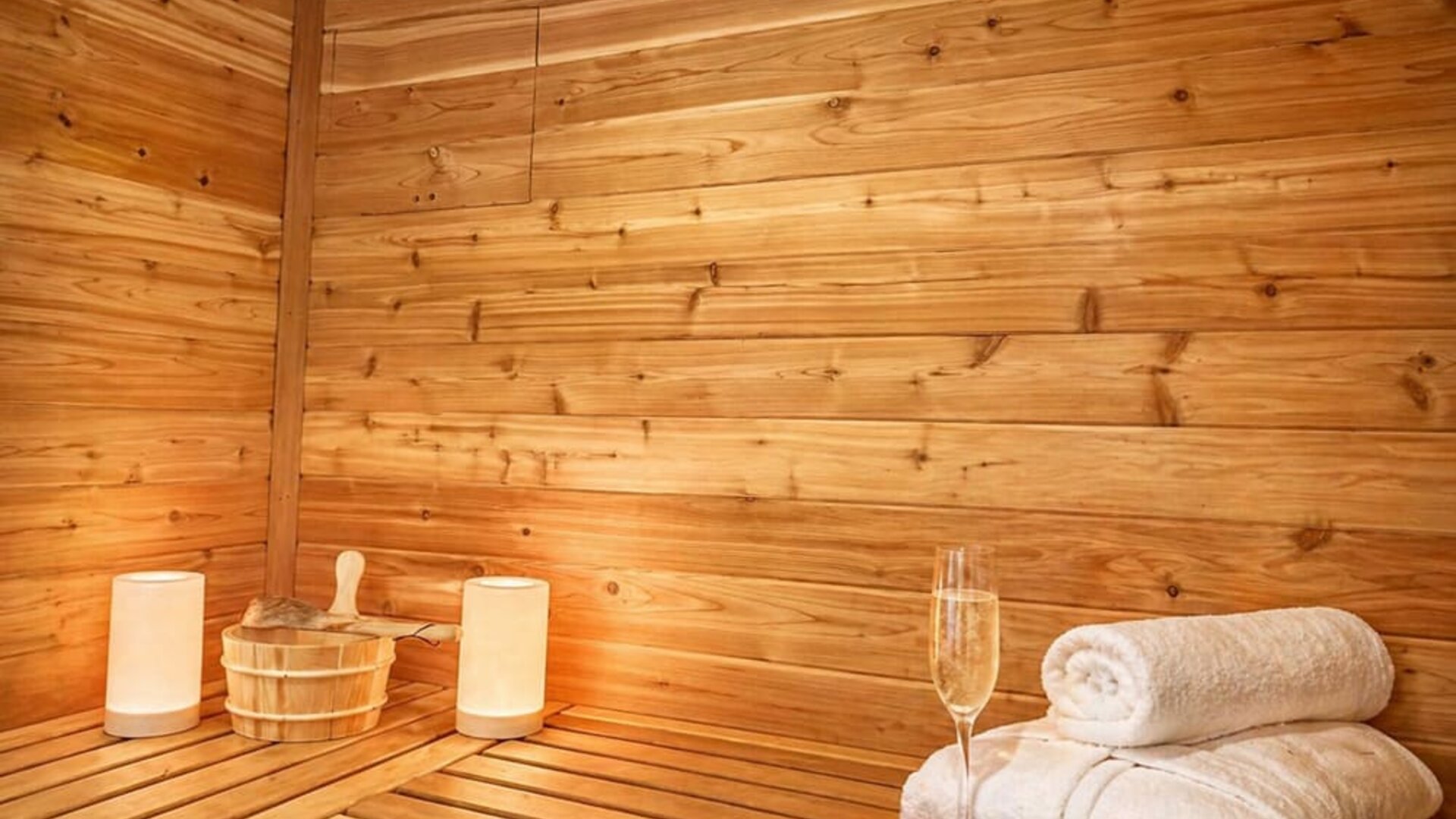 Wood-panelled sauna featuring bench seating, fresh towels, sauna accessories, and ambient lighting at SKYLARANNA Resort & Spa.