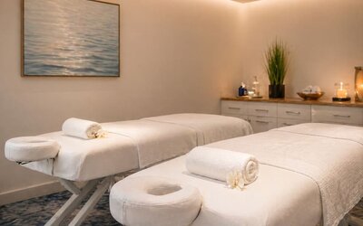 Spa treatment room featuring two massage tables, fresh towels, soft lighting, and contemporary décor at SKYLARANNA Resort & Spa.
