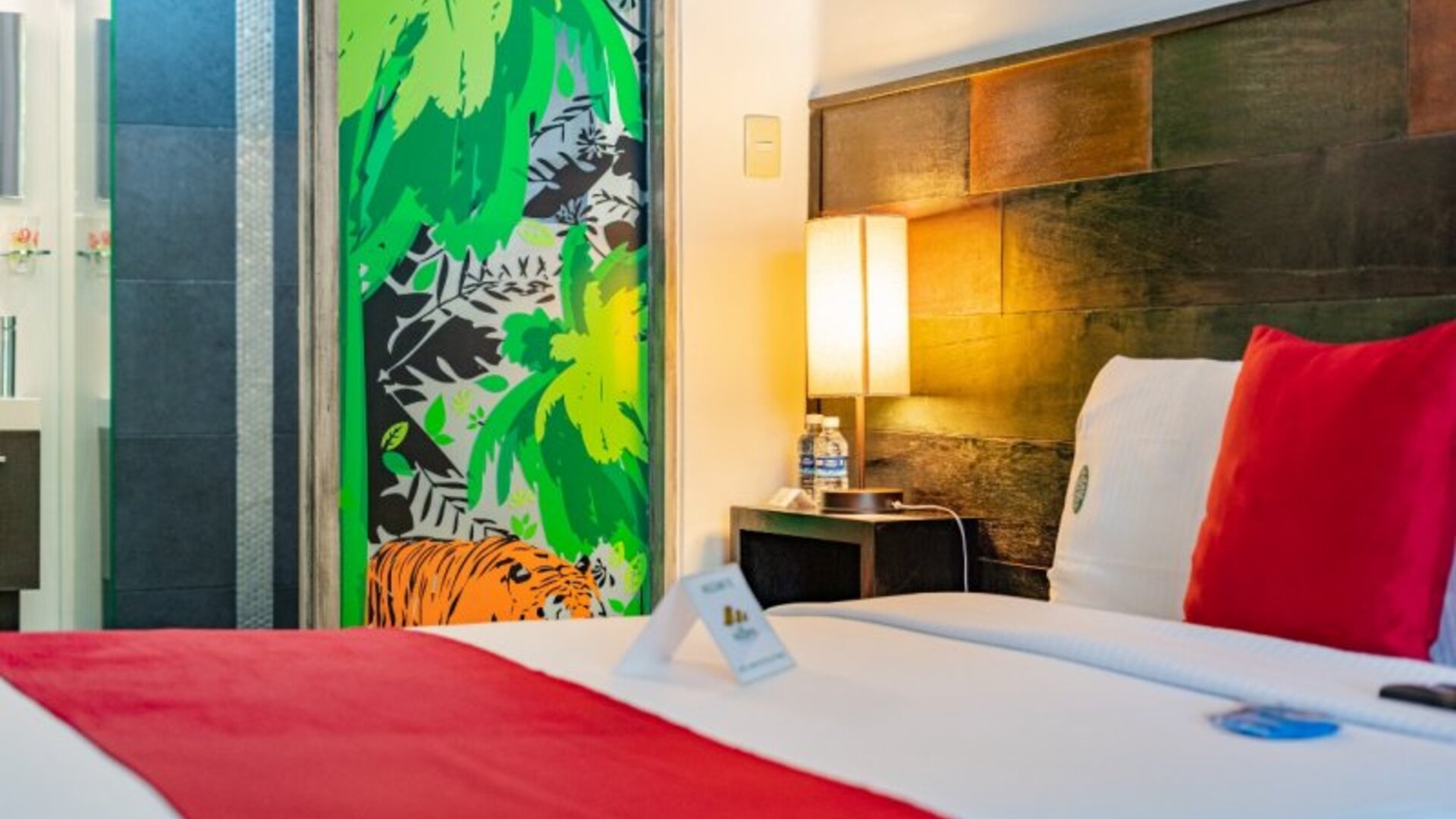 Bright guest room featuring a large bed, exposed brick accent wall, colourful cushions, television, and abundant natural light at Casa Anzures Suites.