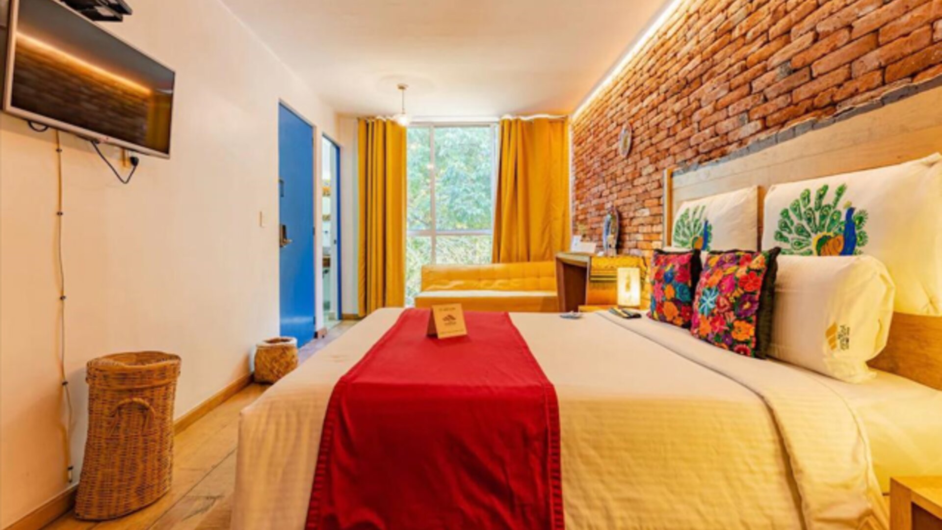 Guest room featuring a comfortable bed, colourful wood-panelled headboard, vibrant tropical artwork, and warm bedside lighting at Casa Anzures Suites.