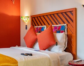 Colourful guest room featuring a comfortable bed, orange accent wall, decorative cushions, and stained-glass-style lighting at Casa Anzures Suites.