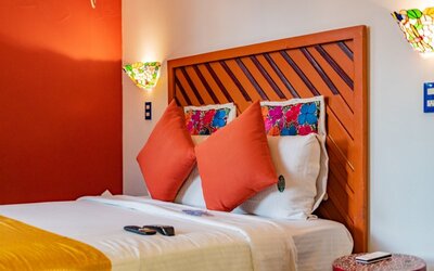 Colourful guest room featuring a comfortable bed, orange accent wall, decorative cushions, and stained-glass-style lighting at Casa Anzures Suites.