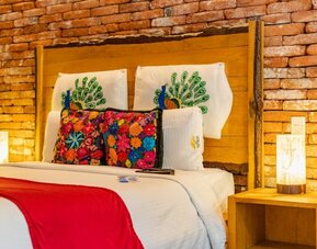 Guest room featuring a large bed, exposed brick accent wall, colourful decorative cushions, and warm bedside lighting at Casa Anzures Suites.