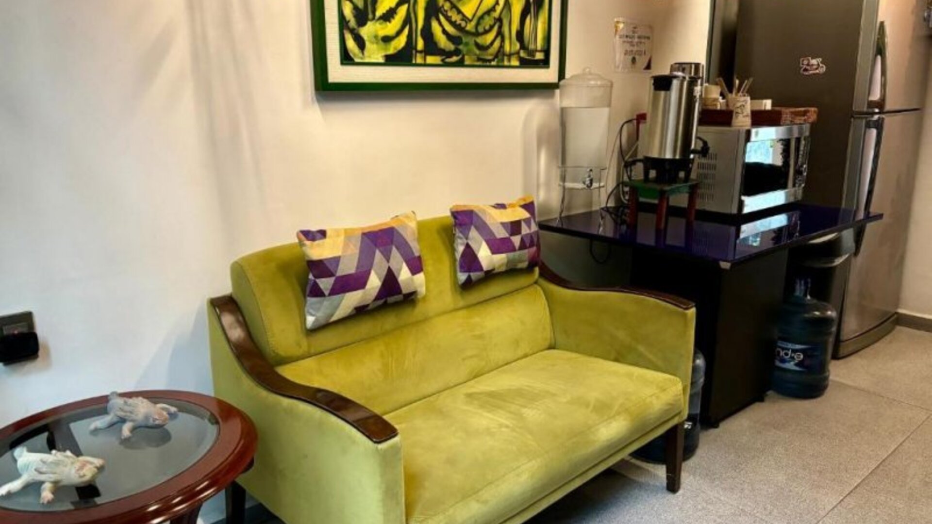 Cosy lounge area featuring a green sofa, decorative cushions, refreshment facilities, and colourful artwork at Casa Anzures Suites.
