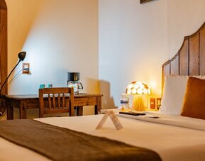 Guest room featuring a comfortable bed, rustic wooden furnishings, bedside lighting, and a dedicated workspace at Casa Anzures Suites.