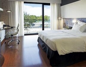 Bright guest room featuring a large bed, television, dedicated workspace, and floor-to-ceiling windows at Hilton Madrid Aeropuerto.