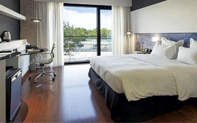 Bright guest room featuring a large bed, television, dedicated workspace, and floor-to-ceiling windows at Hilton Madrid Aeropuerto.