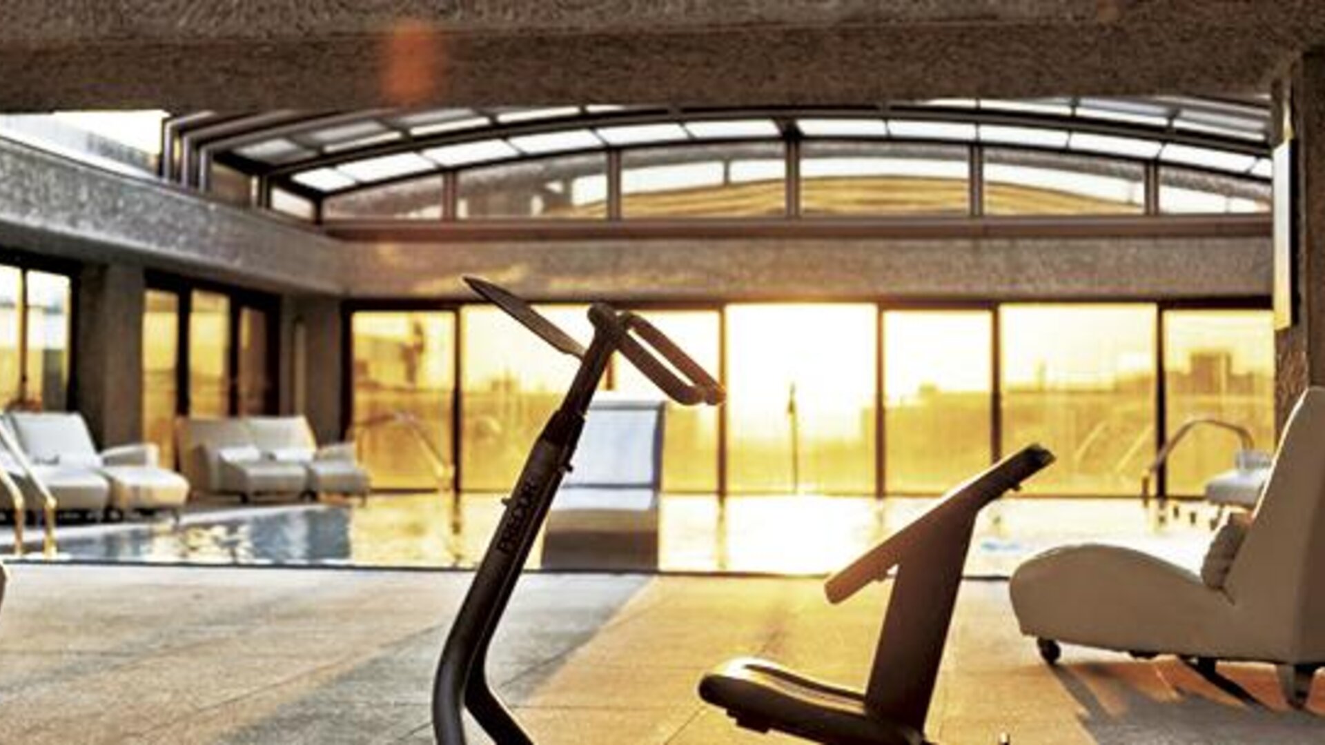 Indoor pool and relaxation area featuring lounge chairs, exercise equipment, and floor-to-ceiling windows at Hilton Madrid Aeropuerto.