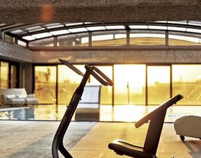 Indoor pool and relaxation area featuring lounge chairs, exercise equipment, and floor-to-ceiling windows at Hilton Madrid Aeropuerto.
