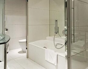 Modern guest bathroom featuring a glass vanity, bathtub, separate glass-enclosed shower, and sleek chrome fixtures at Hilton Madrid Aeropuerto.