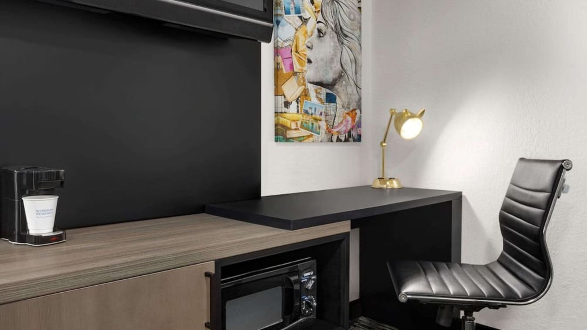 In-room workspace featuring a desk, ergonomic chair, coffee maker, microwave, and contemporary artwork at La Quinta Inn & Suites By Wyndham Cleveland Airport West.