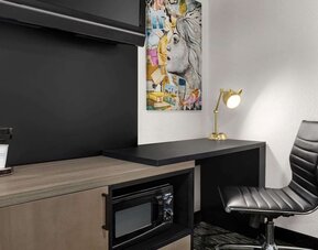 In-room workspace featuring a desk, ergonomic chair, coffee maker, microwave, and contemporary artwork at La Quinta Inn & Suites By Wyndham Cleveland Airport West.
