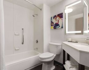 Modern guest bathroom featuring a shower and bathtub combination, illuminated mirror, vanity, fresh towels, and accessibility grab bar at La Quinta Inn & Suites By Wyndham Cleveland Airport West.
