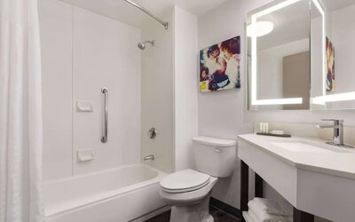 Modern guest bathroom featuring a shower and bathtub combination, illuminated mirror, vanity, fresh towels, and accessibility grab bar at La Quinta Inn & Suites By Wyndham Cleveland Airport West.